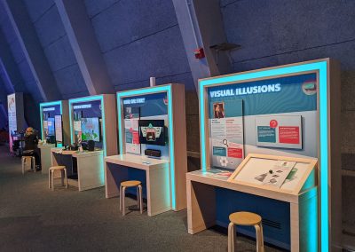 A series of wooden desks and displays in a museum gallery about virtual reality and how it works.