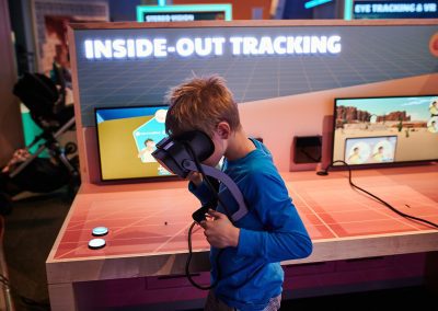 A young boy with a blue shirt looks down as he places a virtual reality headset on and stands in front of a table that says “Inside Out Tracking”