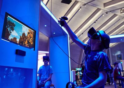 A boy wearing a VR headset reaches up into the air as he experiences an interactive game at a museum.