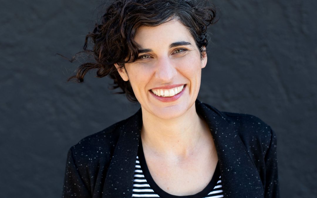 A woman with a striped shirt and a black blazer smiles in a headshot