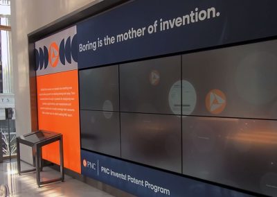 A large wall screen in a bank lobby says, Boring is the mother of invention.
