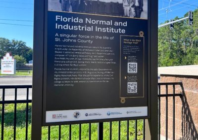 An outdoor sign that shows a photo of a people on the front steps of a school in the early 20th century.