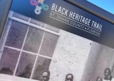 A close-up view of an outdoor sign with a logo that reads, Black Heritage Trail along with a yellow, red, green, and white symbol.