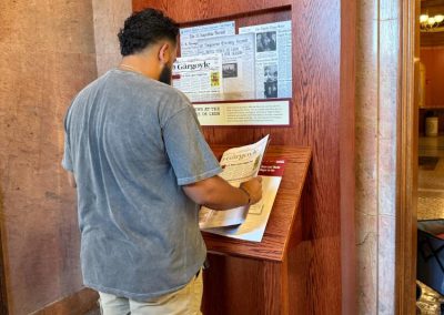 A man with khaki pants and a t-shirt looks through a book at NEWS stand interactive.