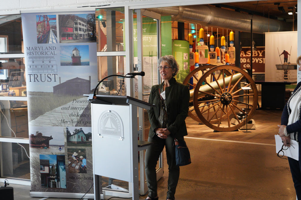 A woman stands in front of a podium and speaks at a museum opening