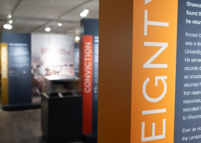 The bright orange edge of a colorful gallery panel in a library. Other freestanding components can be seen in the background.