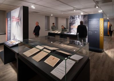 People mill about an exhibition that features rare documents in cases in a library setting.