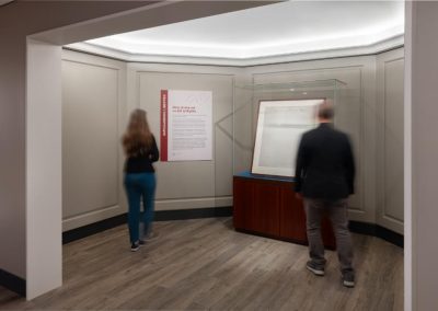 Two people walk through a round gallery nook that contains historic documents.