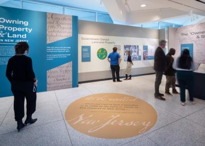 A person stands in a front of a blue wall that says, Owning Land and Property, in a museum exhibit.